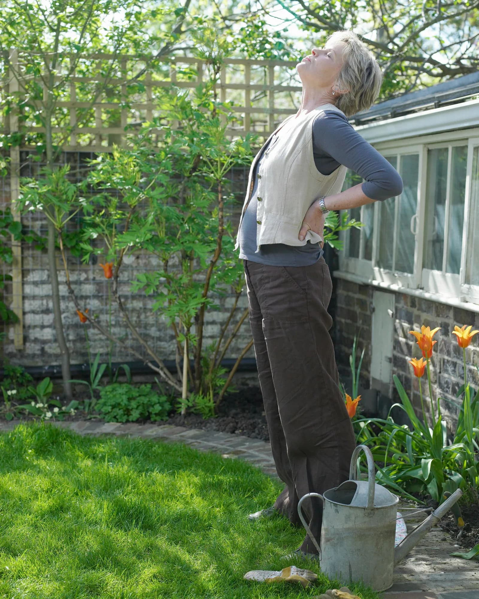 A woman in her garden, stretching in the sun beside a watering can