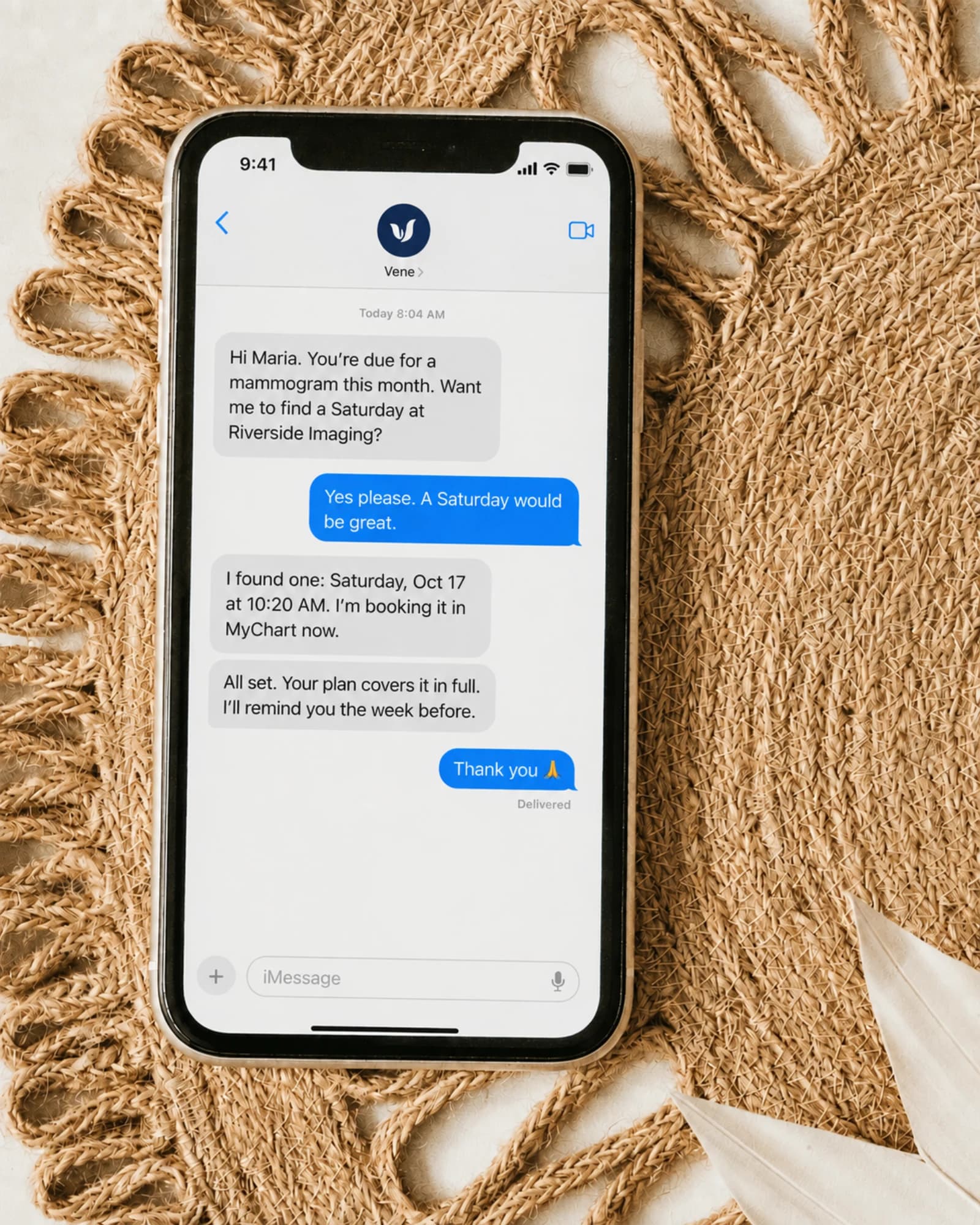 A phone on a woven placemat, seen from above: Vene has texted that a mammogram is due and booked it